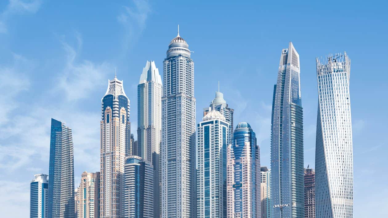 Dubai Marina skyline with modern glass towers and the twisted Cayan Tower under a clear blue sky
