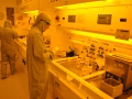 Technicians in cleanroom suits working at photolithography stations under yellow safelight